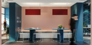 Two red Rail 2 Acoustic luminaires hang in an off lounge area both lights showing illumination above on the ceiling and below on the tables